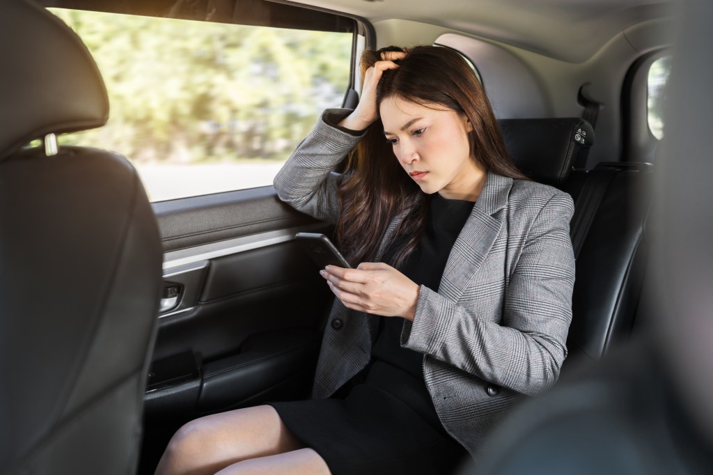 stressed young business woman using a smartphone while sitting in the back seat of the car